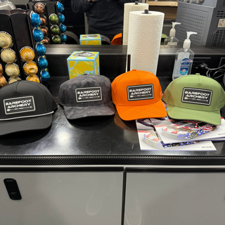 4 hats in black, black camo, orange, and olive green with the barefoot archery logo patch